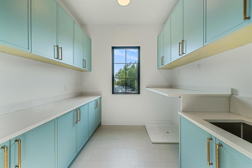 Utility room featuring extensive light blue cabinetry with gold-toned hardware, light-toned countertops, a built-in sink, and a black-framed window