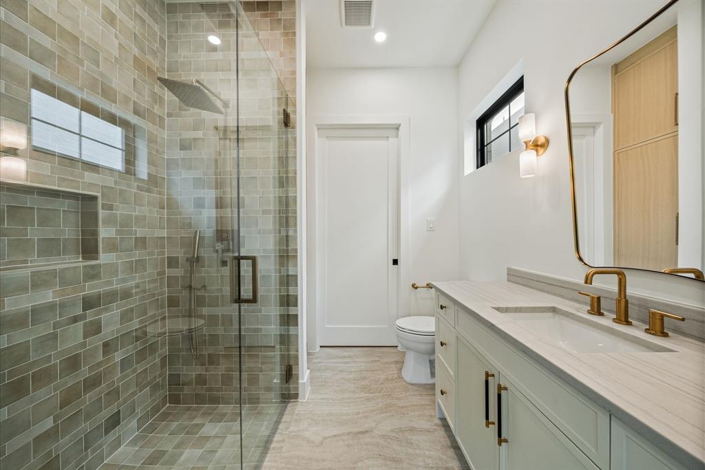 Spa-inspired primary bathroom featuring a frameless glass-enclosed shower with subway tile surround, dual vanity with white quartz countertop, brass fixtures, and wood-finish flooring throughout