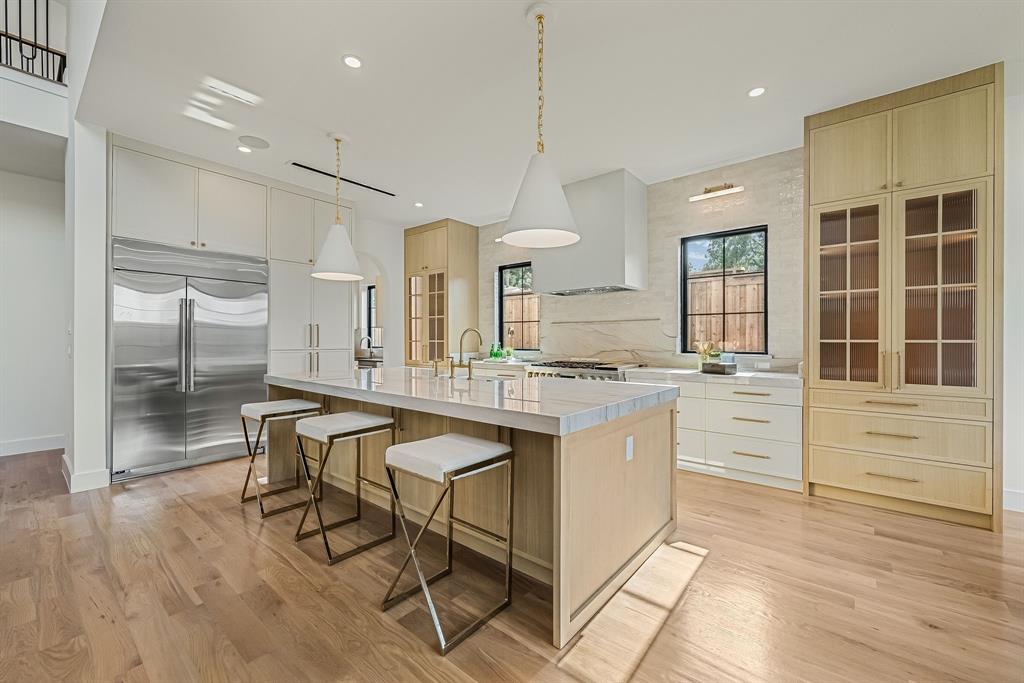 Gourmet kitchen featuring a large central island with seating, stainless steel refrigerator, light wood-finish cabinetry, white countertop surfaces, and wood-finish flooring