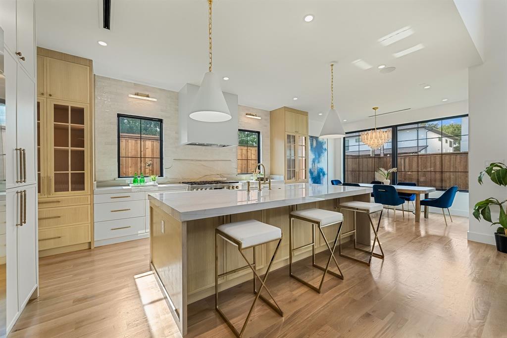 Spacious open-concept kitchen featuring light wood-finish flooring, a large central island with seating, pendant lighting, built-in cabinetry with glass-front accents, and a dining area with a chandelier