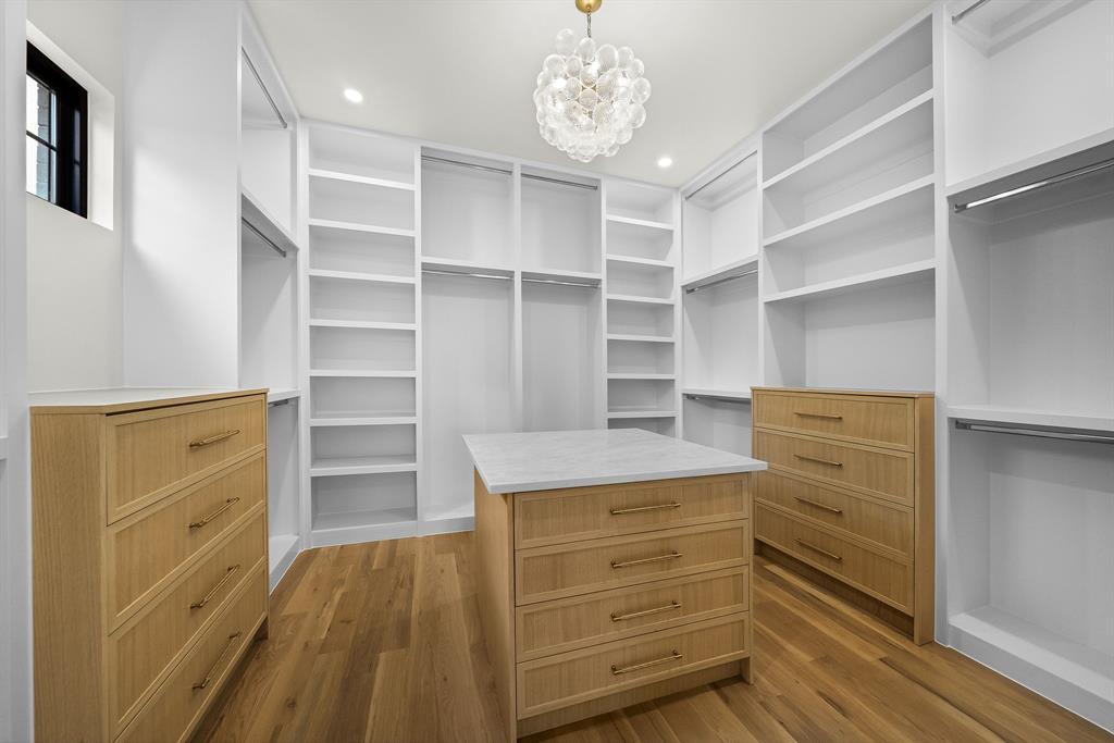 Spacious custom closet featuring extensive built-in shelving, hanging rods, two integrated dressers, a central island with countertop, and wood-finish flooring