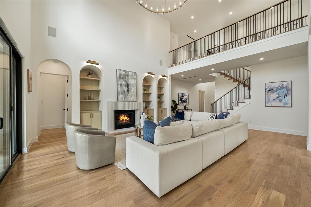 Two-story living area featuring wood-finish flooring, a contemporary fireplace with a vertical tile surround, and arched built-in shelving