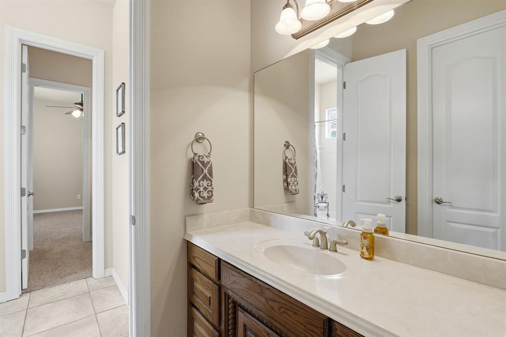 Bathroom vanity featuring a single-bowl sink, light-toned countertop, wood-finish cabinetry, and an expansive wall-mounted mirror