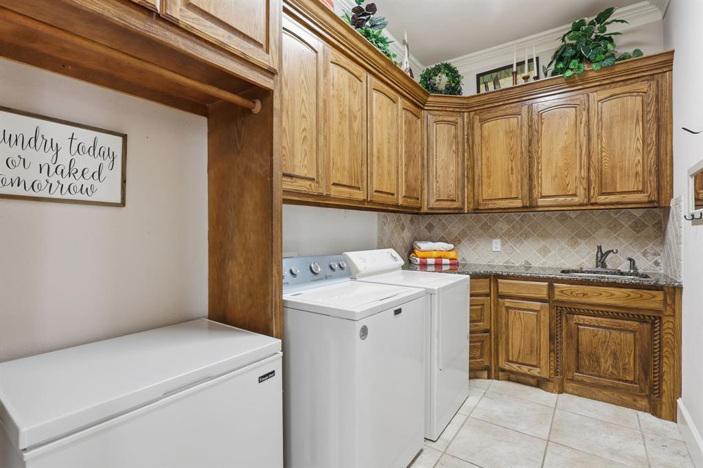 Dedicated utility room featuring wood cabinetry, a built-in sink, stone countertop, tiled backsplash, and tile flooring