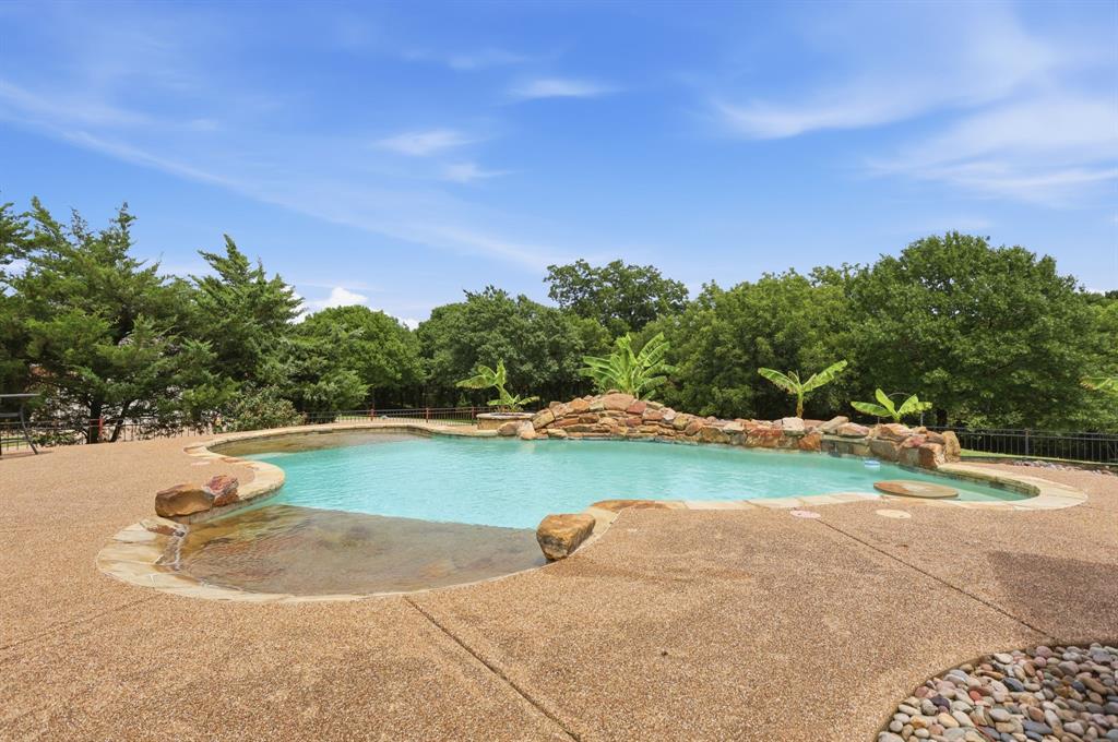 Freeform swimming pool featuring a rock waterfall, integrated spa, and an expansive exposed aggregate patio