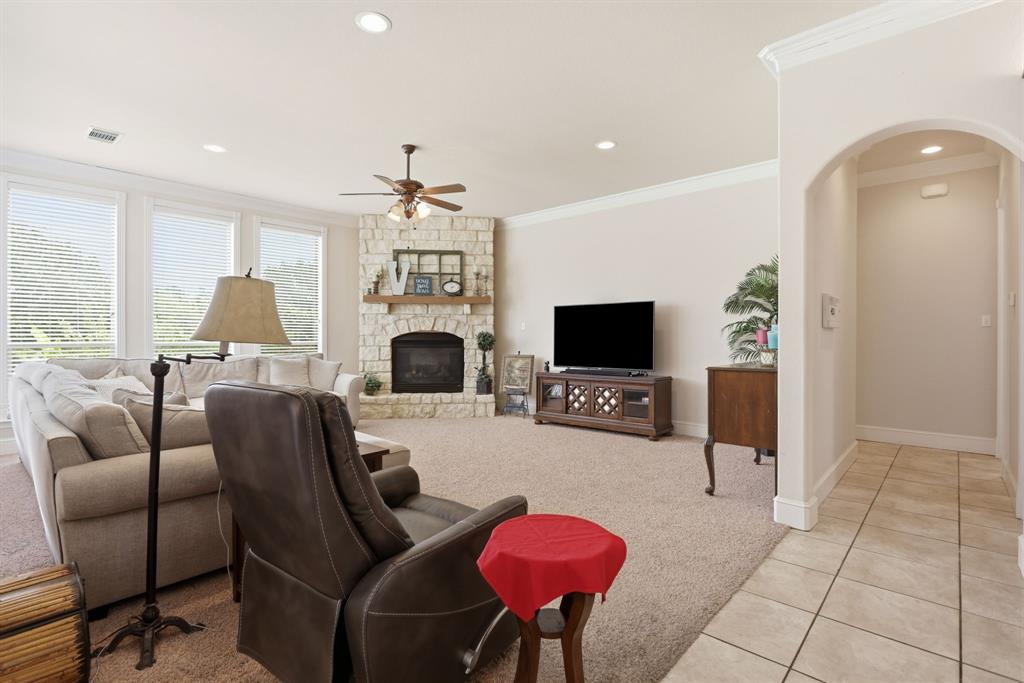 Spacious living area featuring a stone fireplace, crown molding, abundant natural light from multiple windows, recessed lighting, and an arched entryway