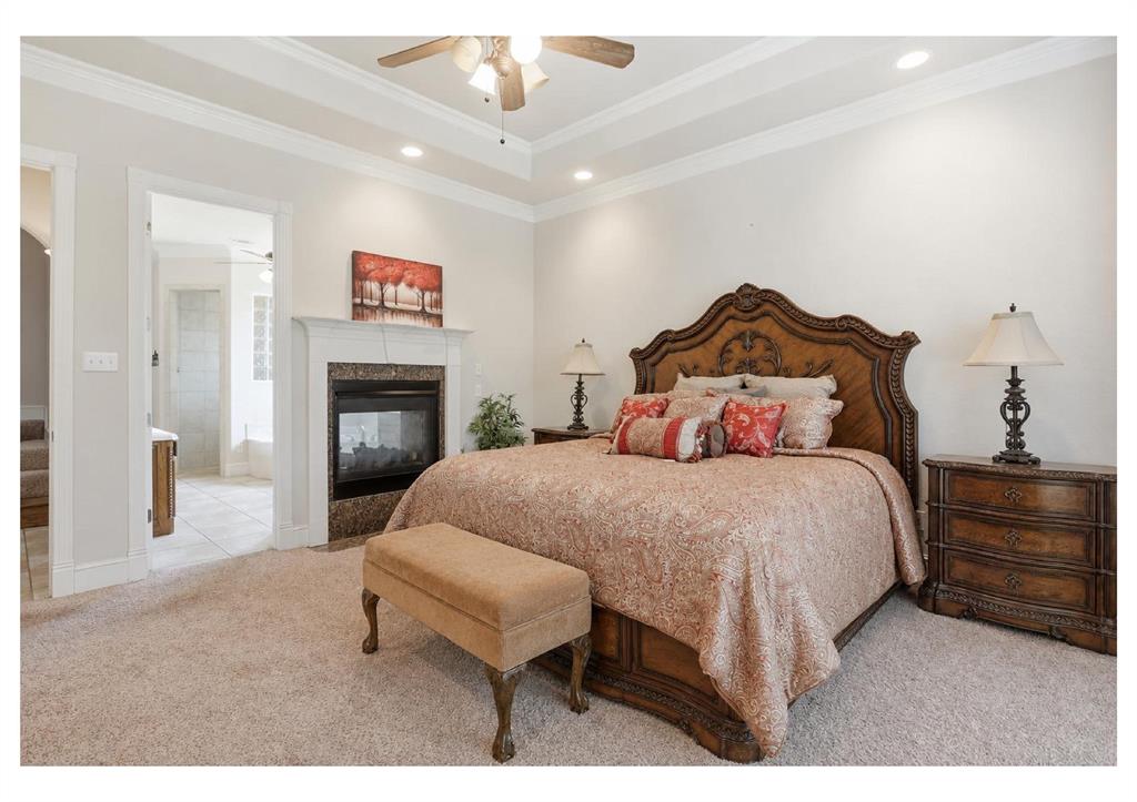 Carpeted bedroom featuring a tray ceiling, recessed lighting, and a built-in fireplace with a stone surround