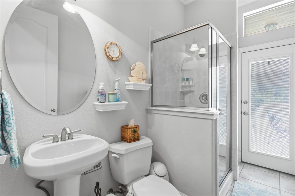 Pedestal sink with a brushed nickel faucet, large oval mirror, glass-enclosed shower with tiled walls, and a full-light exterior door