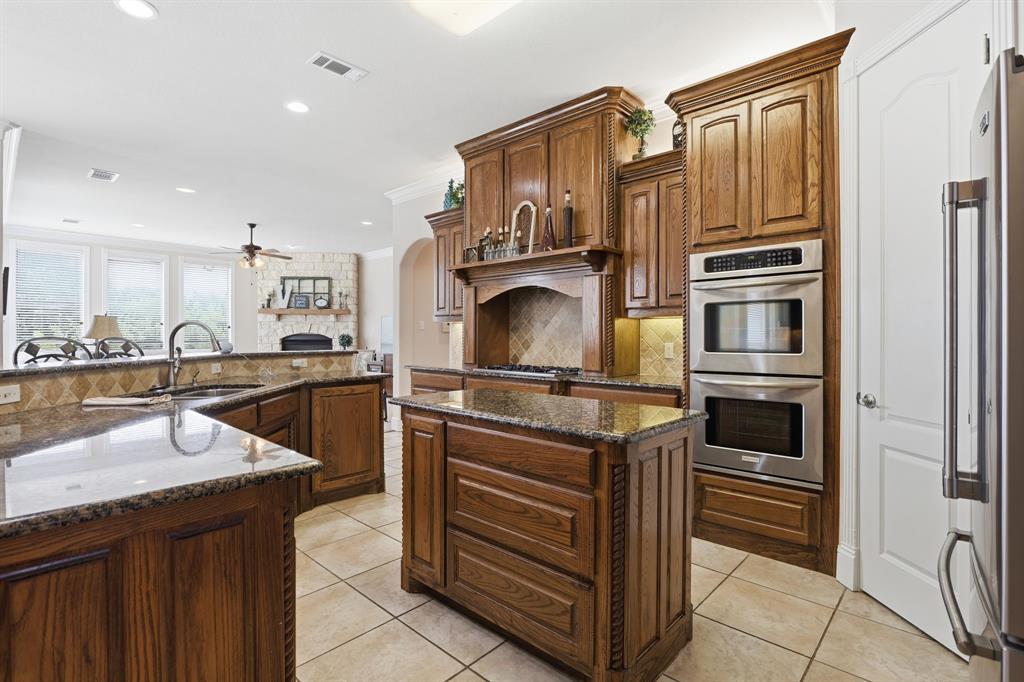 Kitchen featuring rich wood cabinetry, granite countertops, a central island, stainless steel double ovens, and tile flooring