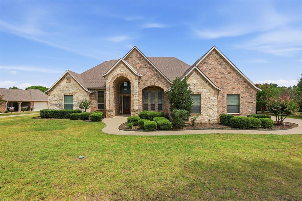 Brick and stone facade residence featuring a covered entry, arched windows, and a concrete pathway leading to the front door