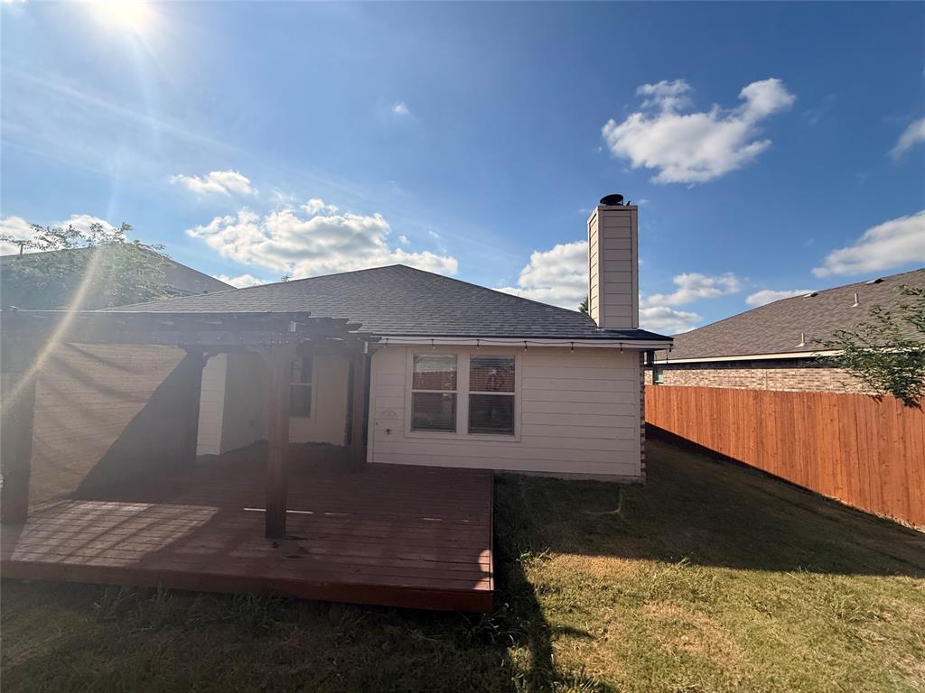 Expansive backyard featuring a wood deck with a pergola, a sloped grassy area, a wooden privacy fence, and a visible chimney