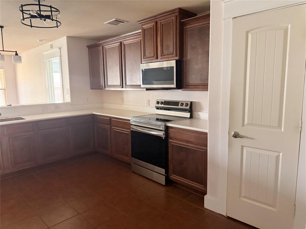 Kitchen featuring wood-finish cabinetry, light-toned countertops, and stainless steel appliances including a range and built-in microwave
