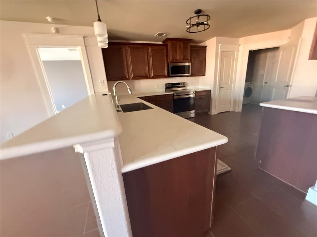 Kitchen featuring a stainless steel sink with gooseneck faucet, light-toned countertops, and rich wood-finish cabinetry Kitchen featuring a stainless steel sink with gooseneck faucet, light-toned countertops, and rich wood-finish cabinetry