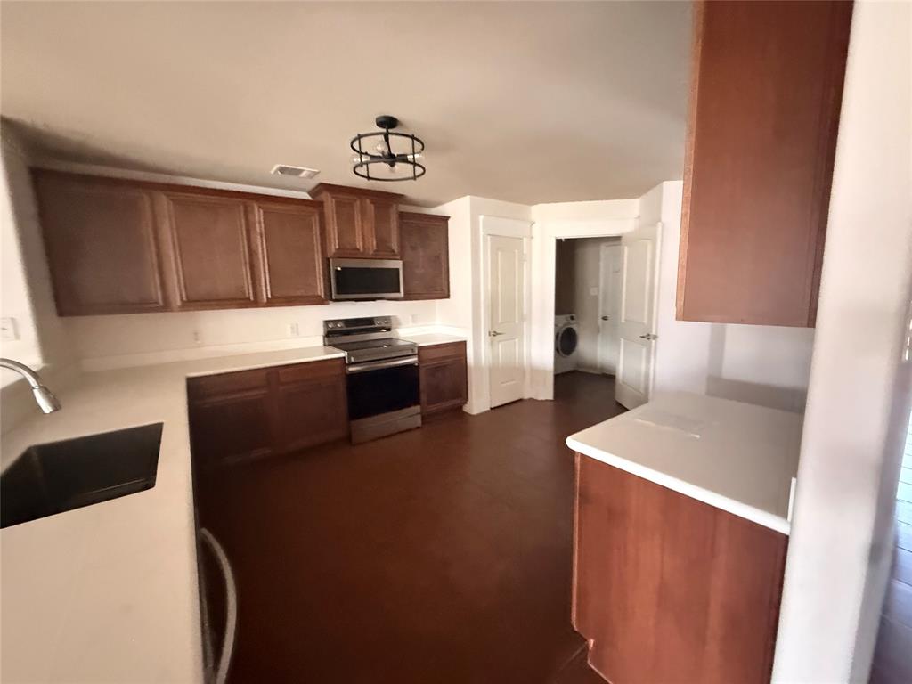 Kitchen featuring wood-finish flooring, white countertops, dark wood cabinetry, and stainless steel appliances including an oven range and microwave