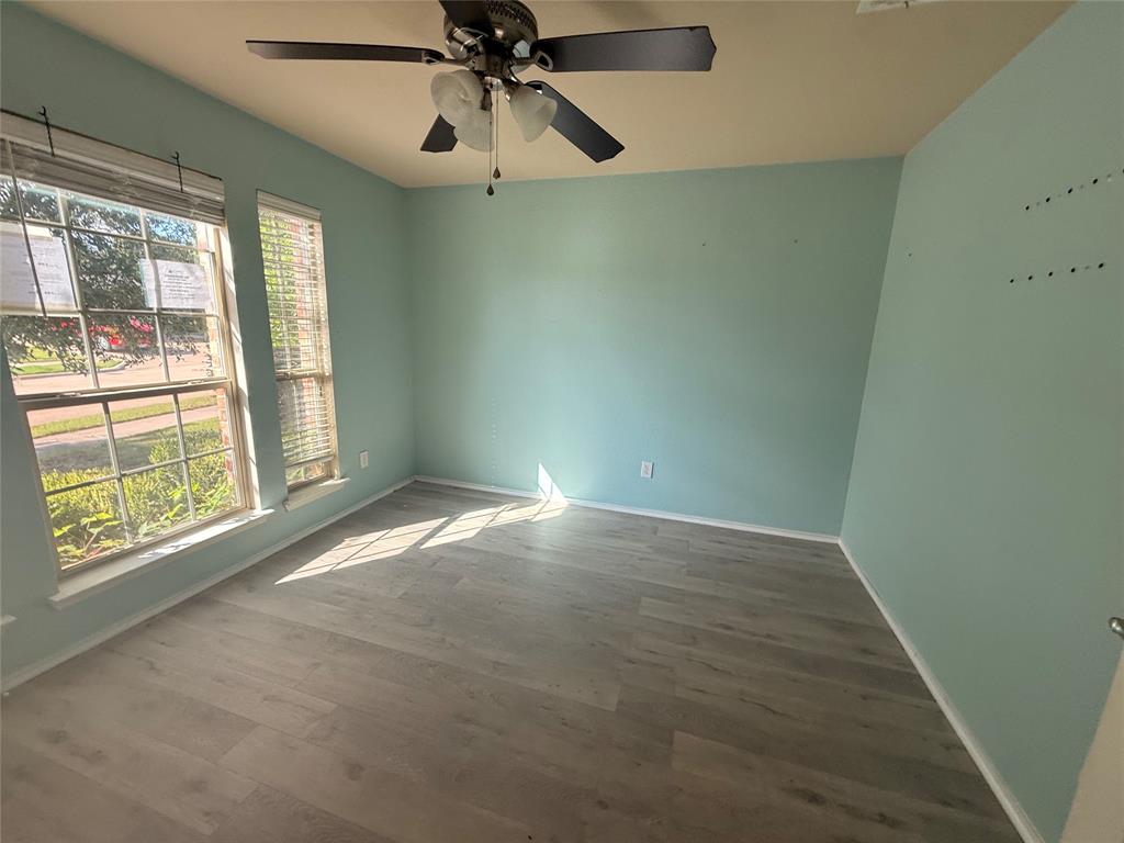 Room featuring wood-finish flooring, two large windows with blinds, a ceiling fan with integrated lighting, and light blue wall finishes Room featuring wood-finish flooring, two large windows with blinds, a ceiling fan with integrated lighting, and light blue wall finishes