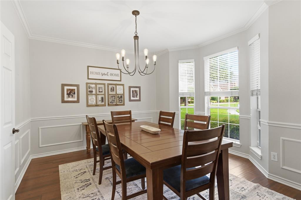 Dedicated dining area featuring a bay window with multiple panes, wood-finish flooring, wainscoting with decorative trim, crown molding, and a central chandelier