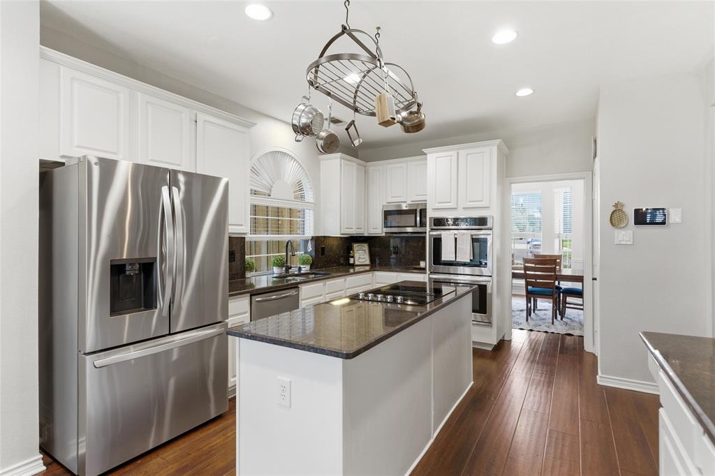 Gourmet kitchen featuring white cabinetry, stainless steel appliances, dark stone countertops, wood-finish flooring, and a central island with a cooktop Gourmet kitchen featuring white cabinetry, stainless steel appliances, dark stone countertops, wood-finish flooring, and a central island with a cooktop