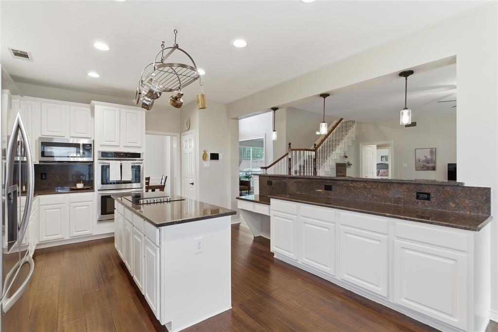Kitchen featuring white cabinetry, dark stone countertops, stainless steel appliances, wood-finish flooring, and a central island with cooktop