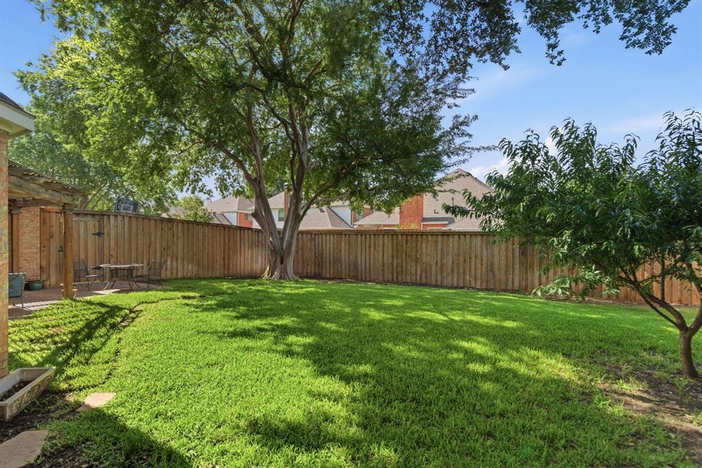 Expansive backyard featuring a large tree, lush green lawn, private wood fencing, and a brick patio with a pergola structure
