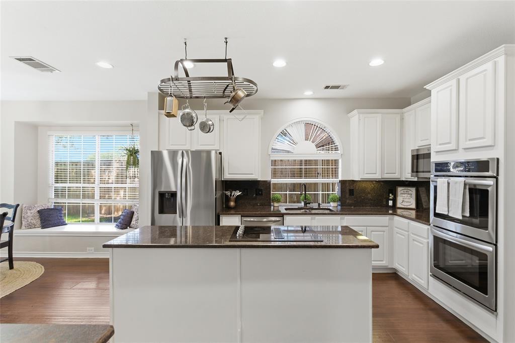 White cabinetry kitchen featuring a central island, stainless steel appliances, dark countertops, and wood-finish flooring White cabinetry kitchen featuring a central island, stainless steel appliances, dark countertops, and wood-finish flooring