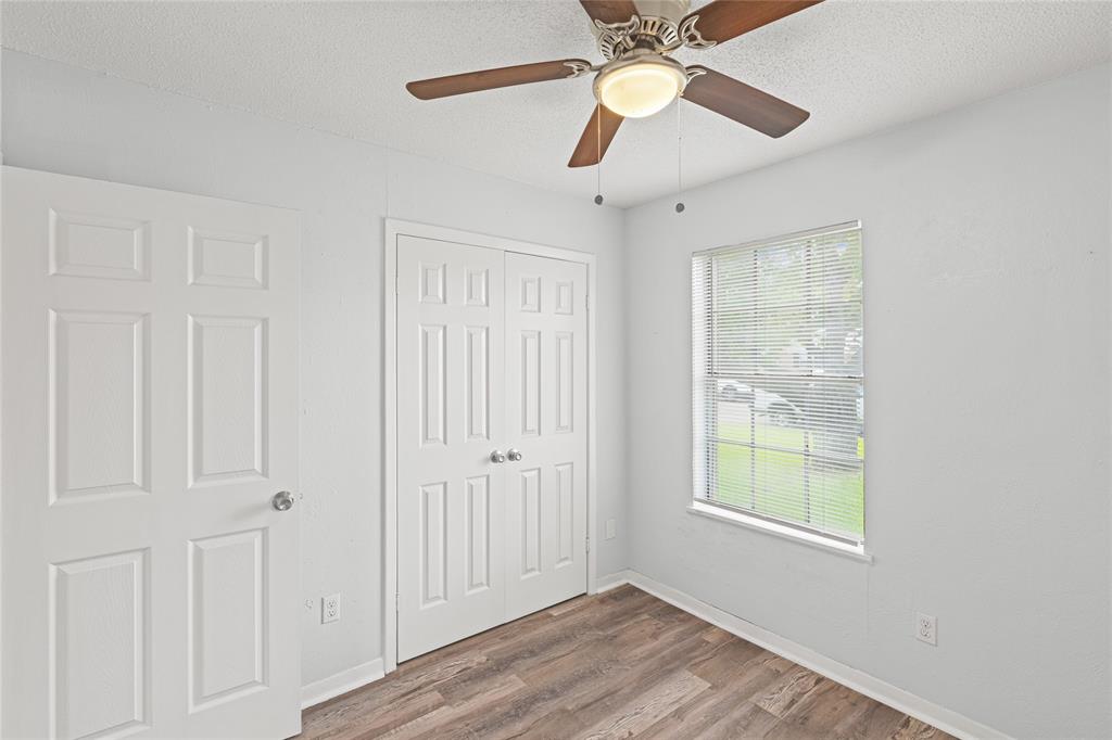 Interior space featuring wood-finish flooring, a white window with blinds, and a ceiling fan with integrated lighting