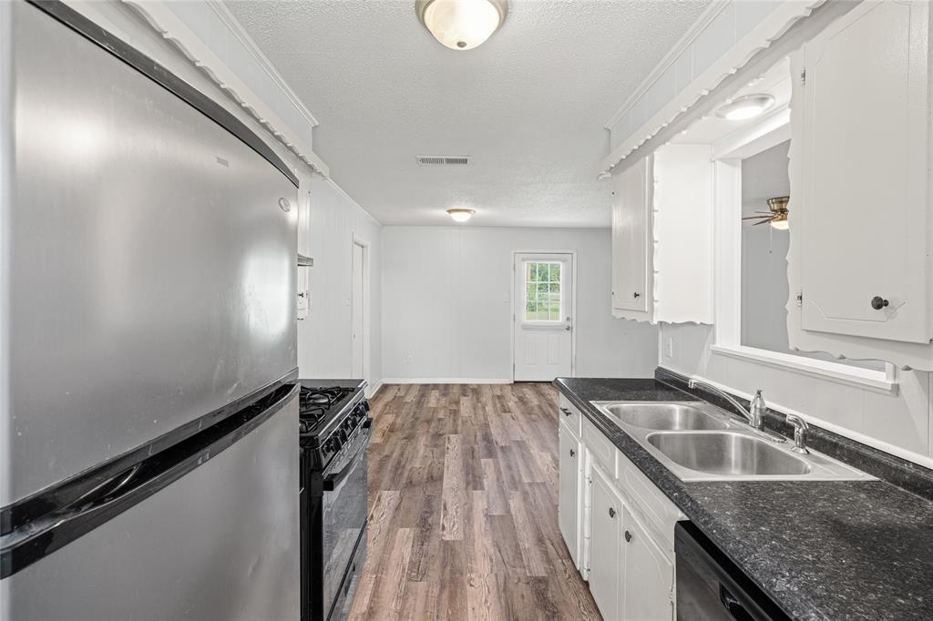 Kitchen featuring a stainless steel refrigerator, black gas range, dual basin stainless steel sink, black countertops, and white cabinetry