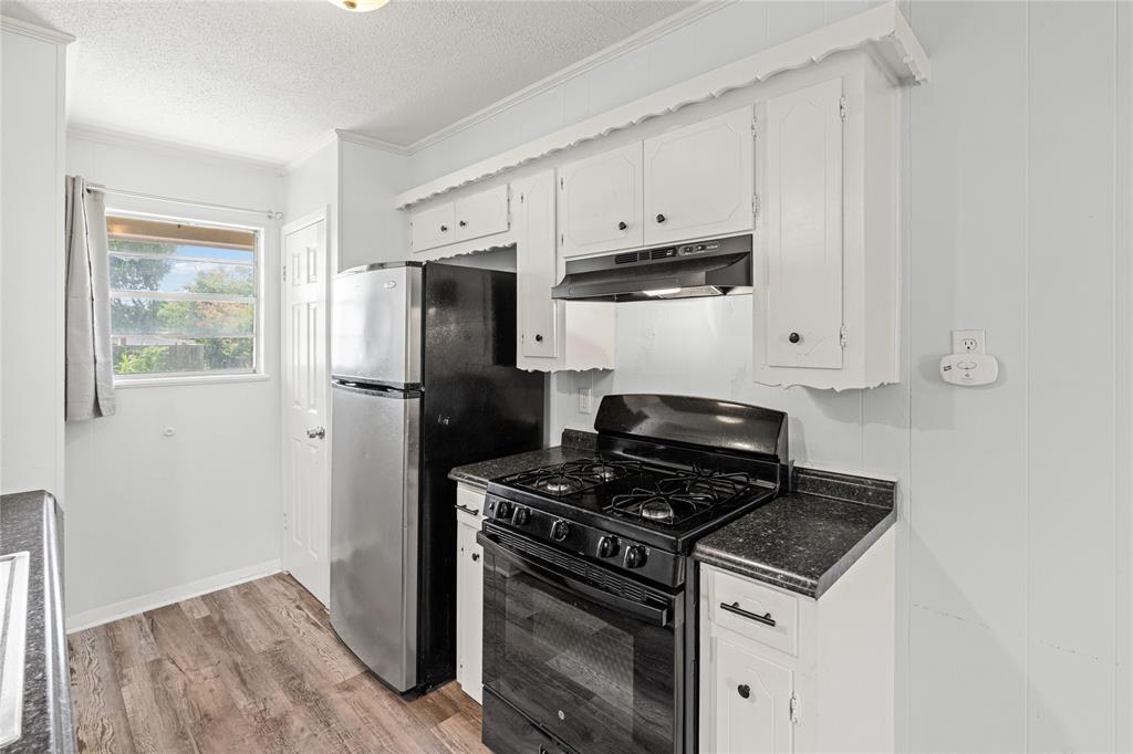 Kitchen featuring white cabinetry, black countertops, a stainless steel refrigerator, a black gas range, and wood-finish flooring