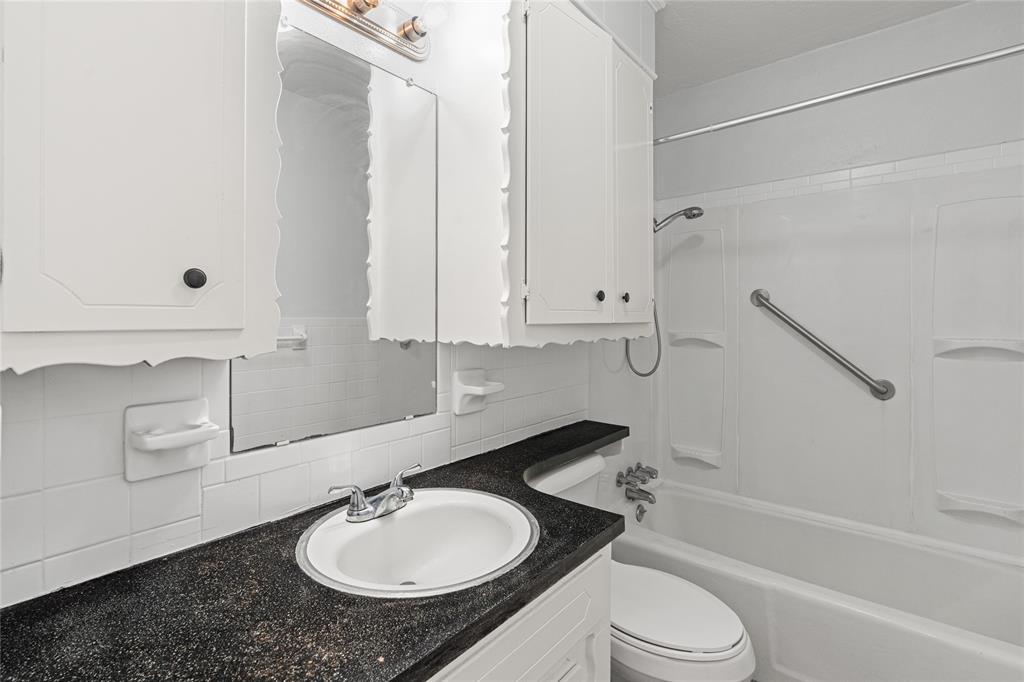 White bathroom featuring a built-in tub with a shower head, grab bar, and wall-mounted shower caddy
