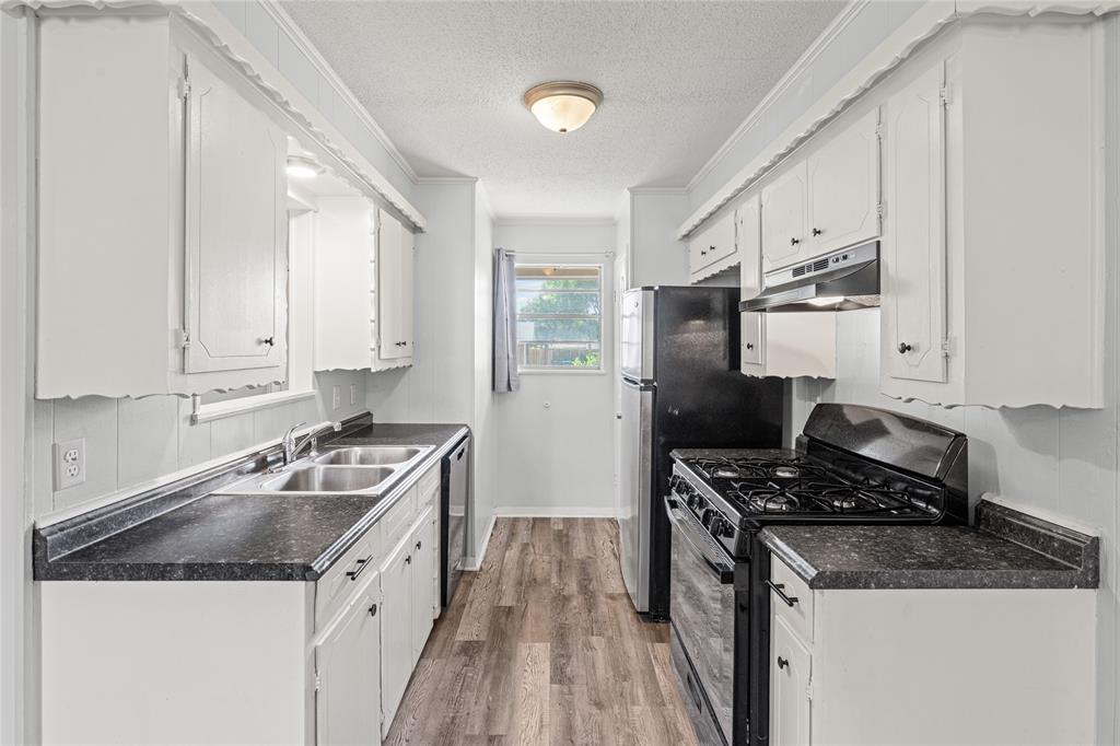 Galley kitchen featuring white cabinetry, dark countertops, wood-finish flooring, and a window for natural light