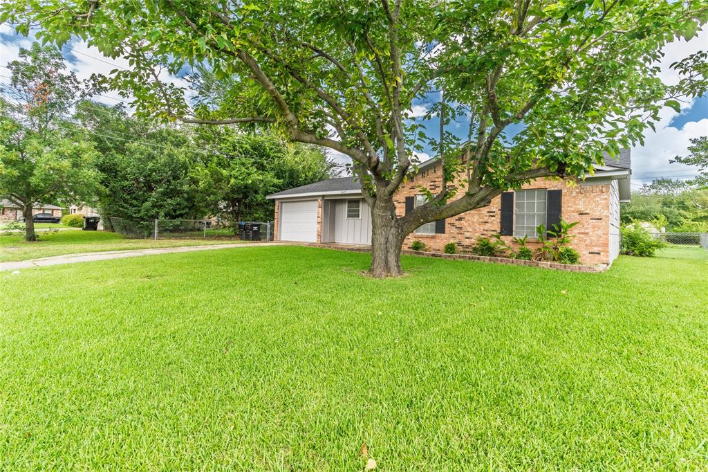 Expansive front yard with a mature shade tree, a brick exterior, and a single-car garage