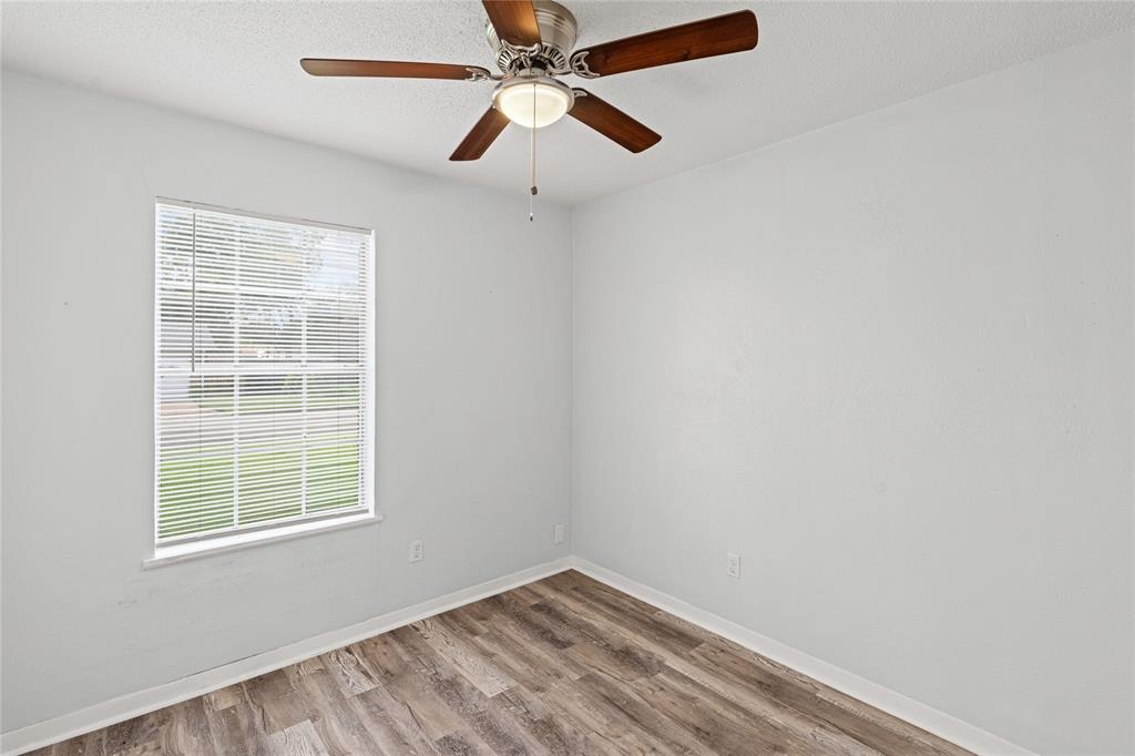 Room featuring wood-finish flooring, a ceiling fan with integrated lighting, and a window with blinds