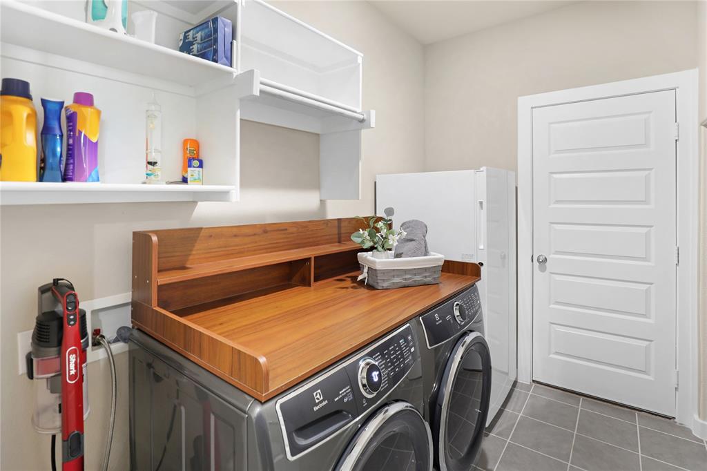 Dedicated laundry area featuring a wood-finish countertop, integrated shelving, and white overhead cabinetry