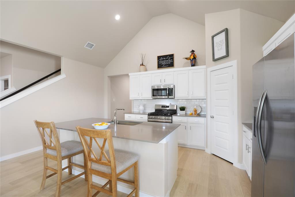 Modern kitchen featuring a central island with integrated sink, stainless steel appliances, white cabinetry, and a subway tile backsplash