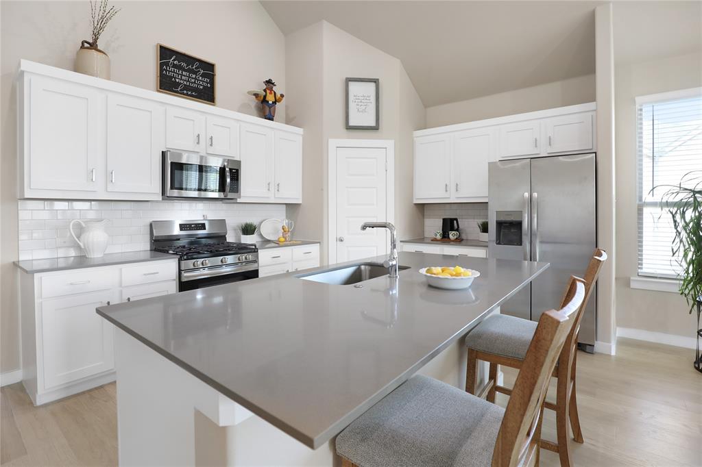Spacious kitchen featuring white cabinetry, stainless steel appliances, a light-toned subway tile backsplash, and a large island with a double basin sink and extended countertop seating