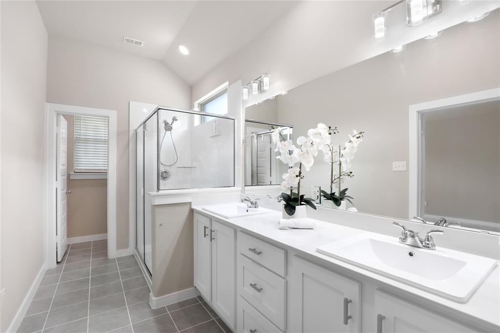 Spacious bathroom featuring a dual vanity with white cabinetry and integrated sinks, a walk-in glass-enclosed shower, tile flooring, and a vaulted ceiling