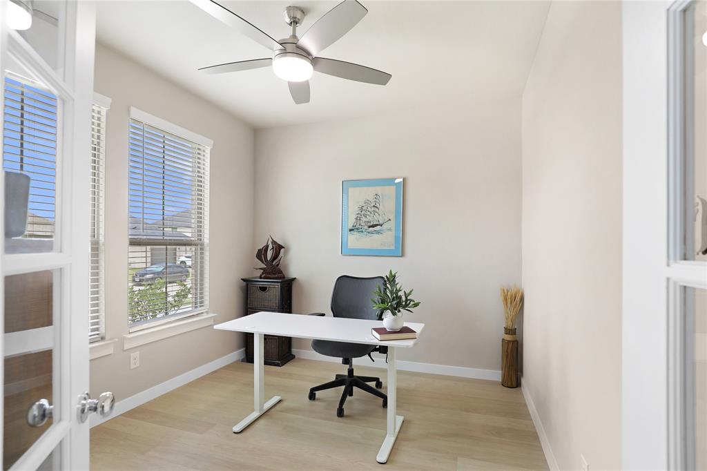 Versatile room featuring two large windows with blinds, light wood-finish flooring, and a ceiling fan with integrated lighting