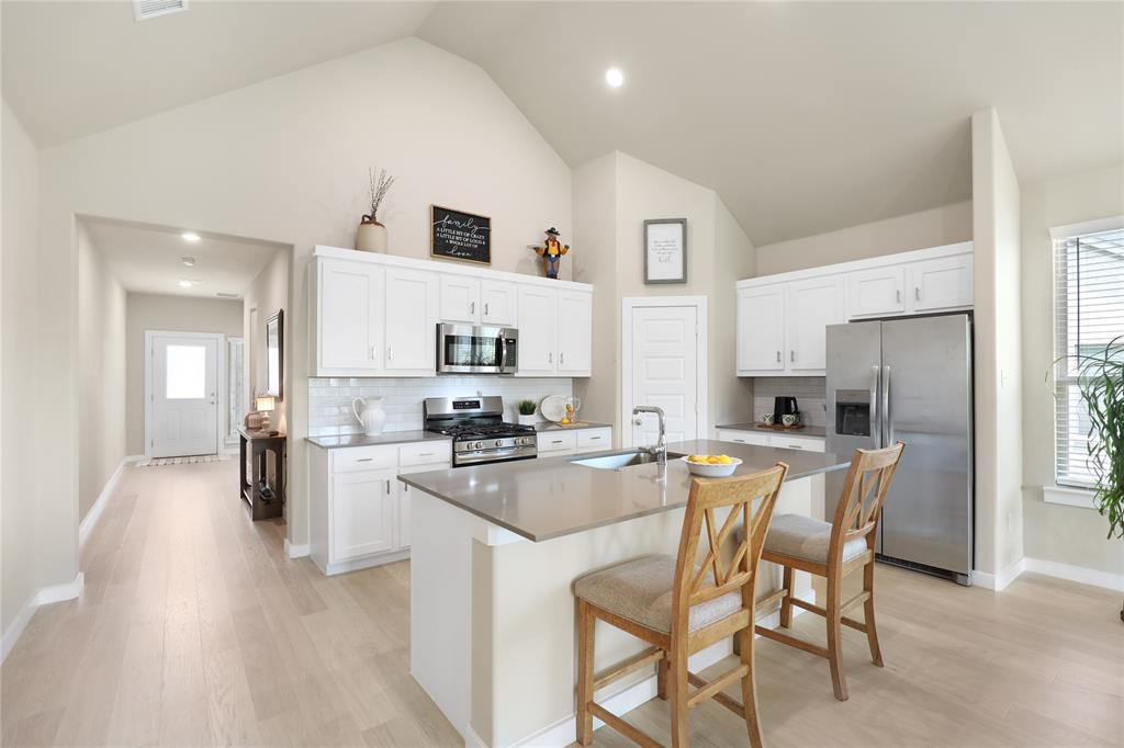 Kitchen featuring a vaulted ceiling, white shaker cabinetry, stainless steel appliances, a center island with sink, and wood-finish flooring