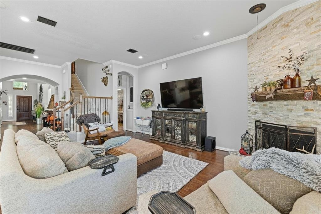 Living room with hardwood-finish flooring, recessed lighting, and a stone-clad fireplace featuring a wood mantle Living room with hardwood-finish flooring, recessed lighting, and a stone-clad fireplace featuring a wood mantle