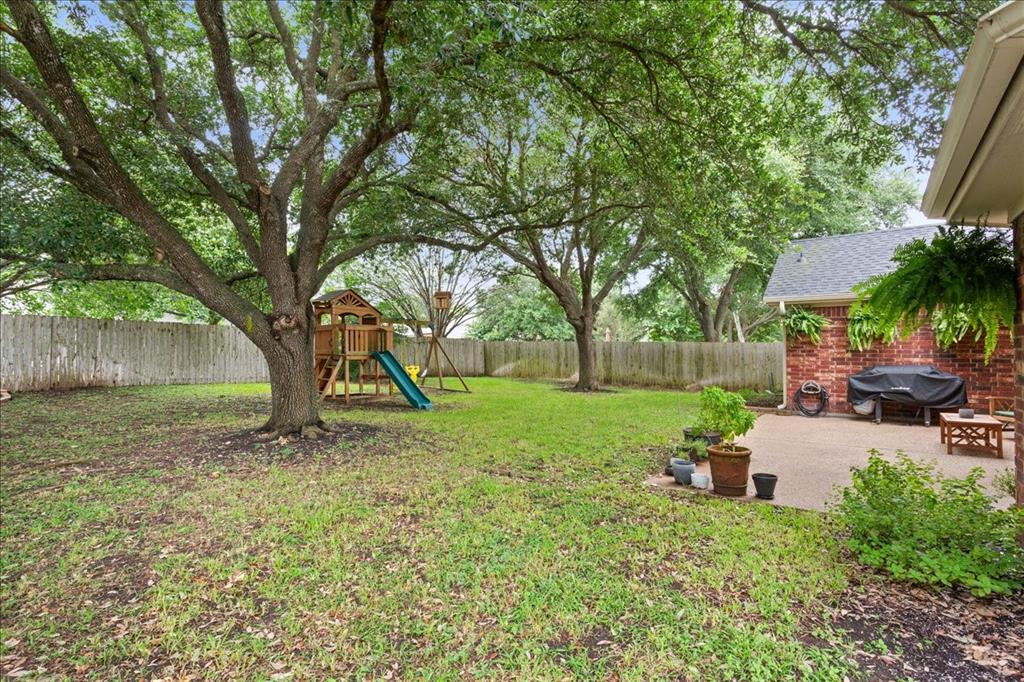Expansive backyard featuring mature trees, a wooden privacy fence, a brick exterior with a dark shingle roof, and a concrete patio