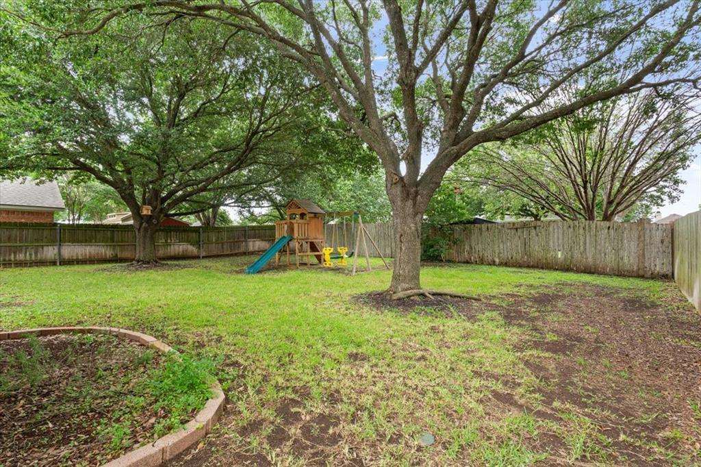 Expansive backyard featuring mature trees, a wooden privacy fence, and a defined garden bed with brick edging