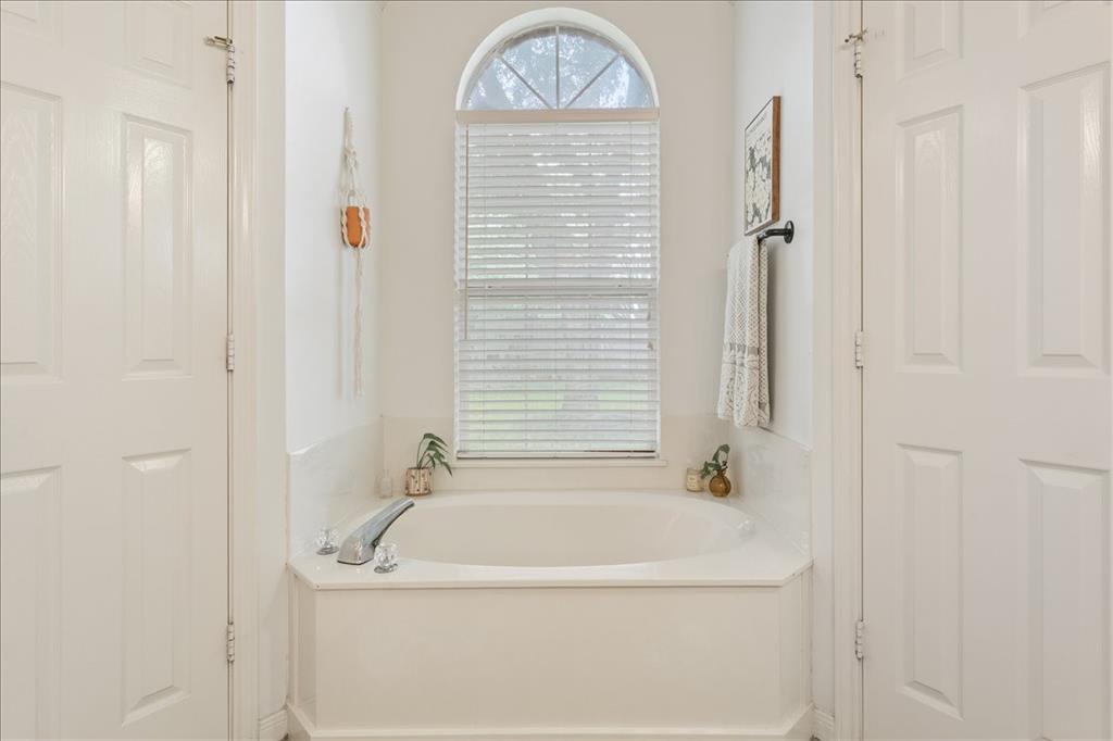 Soaking tub with chrome fixtures, arched window with horizontal blinds, and white paneled doors