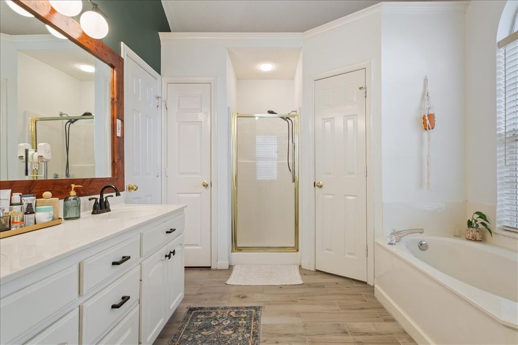 Bathroom featuring a white vanity with black hardware, a wood-framed mirror, a built-in bathtub, a glass-enclosed shower, and wood-finish flooring