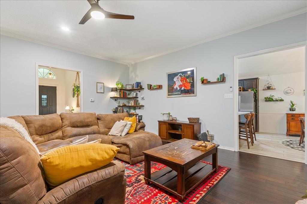 Living area featuring dark wood-finish flooring, light-toned walls, a modern ceiling fan, and open doorways Living area featuring dark wood-finish flooring, light-toned walls, a modern ceiling fan, and open doorways