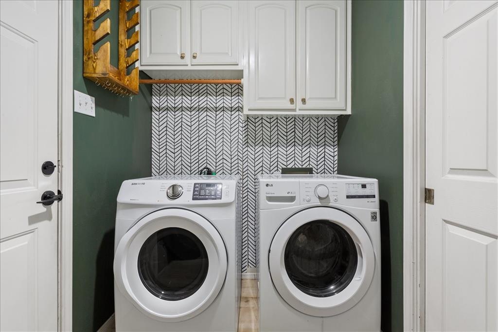 Dedicated laundry area featuring a patterned backsplash, overhead cabinetry with brass-finish hardware, a wooden hanging rod, and contrasting accent wall