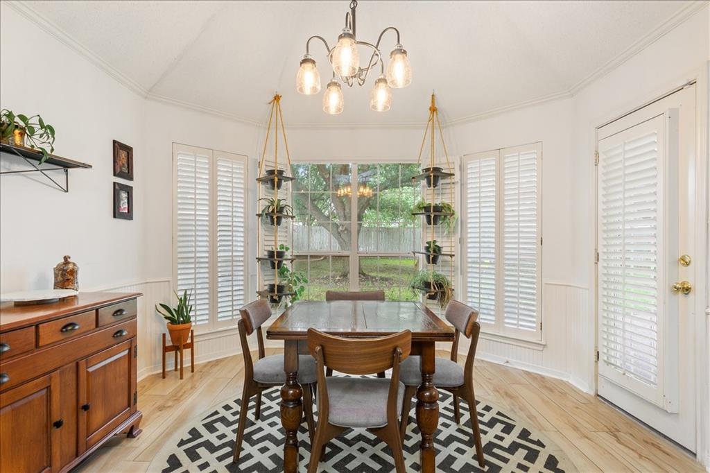 Tray ceiling with a five-light chandelier, wood-finish flooring, white paneling, and an exterior door with louvered blinds
