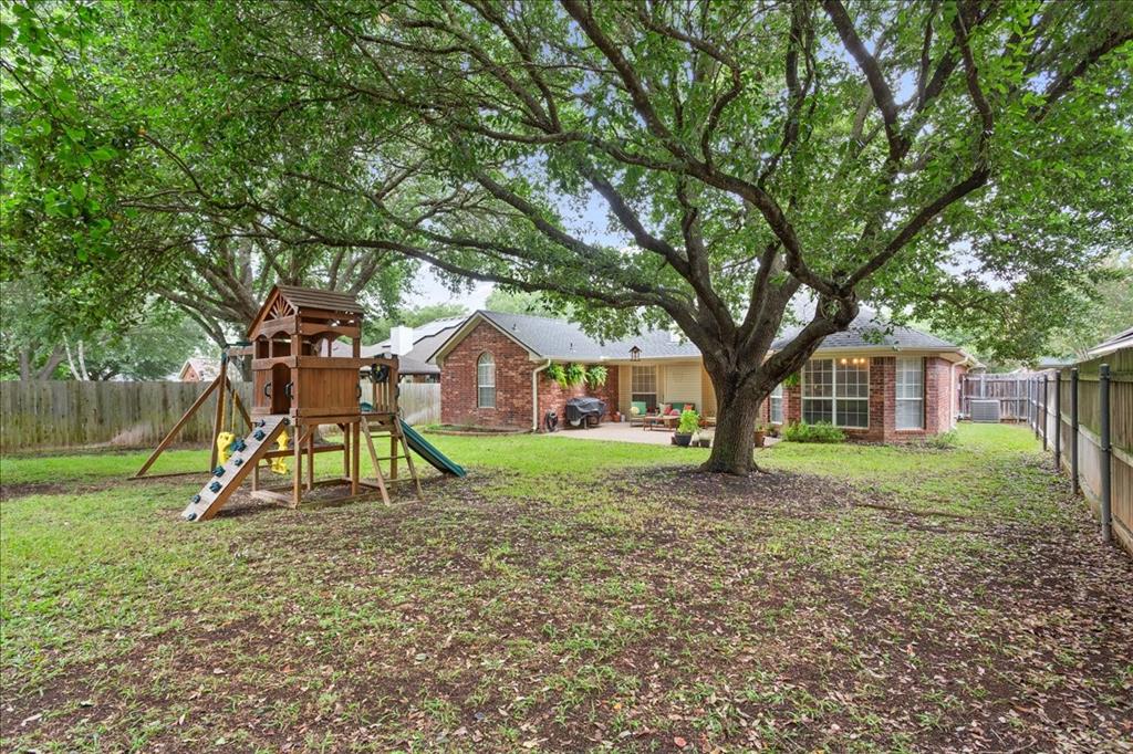 Expansive fenced backyard featuring a large mature tree providing natural shade, a brick exterior, and a concrete patio
