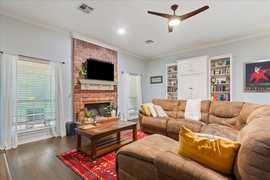 Living area featuring a brick fireplace with a white mantel, wood-finish flooring, built-in shelving, and crown molding Living area featuring a brick fireplace with a white mantel, wood-finish flooring, built-in shelving, and crown molding