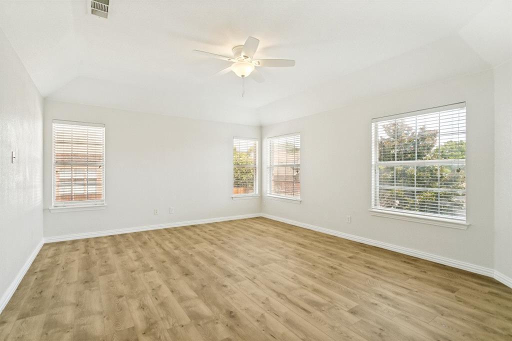 Spacious room featuring wood-finish flooring, vaulted ceiling, and a ceiling fan with light fixture