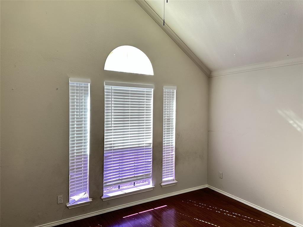 Vaulted ceiling with crown molding, arched transom window, two vertical windows with blinds, and wood-finish flooring