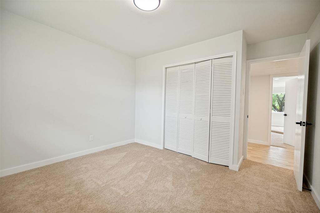 Spacious room featuring neutral carpeting, white baseboards, and a white interior door with black hardware